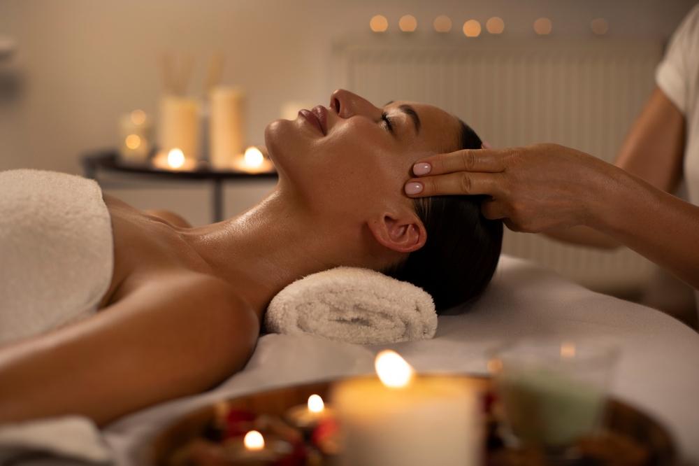 Una donna si gode un rilassante massaggio antistress alla testa e si fa coccolare nella calda atmosfera a lume di candela di un salone spa in un resort o hotel di lusso.